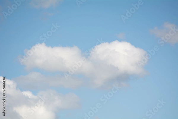 Fototapeta Soft white clouds drift across a clear blue sky during a sunny afternoon