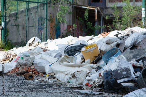 Fototapeta Pile of discarded construction materials and waste near abandoned building in urban area