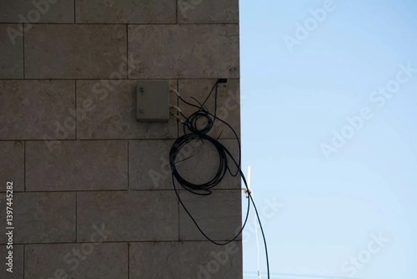 Fototapeta Utility cables hang on a building wall under clear blue sky during daytime in an urban setting