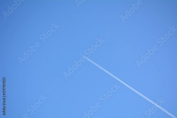 Fototapeta Clear blue sky with a high-flying airplane leaving a contrail during midday