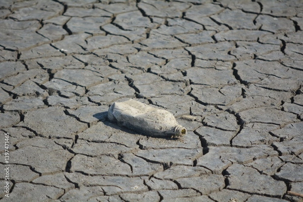 Fototapeta Plastic bottle on dry cracked earth in an arid area highlighting environmental pollution and drought conditions