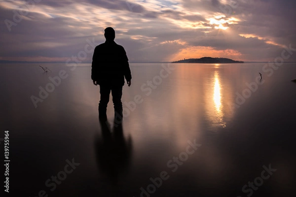 Fototapeta Long exposure shot of a silhouette of a man in water in front of a sunset