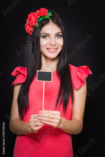 Fototapeta Beautiful woman with a wreath of red flowers holds a wooden plaque. Close-up