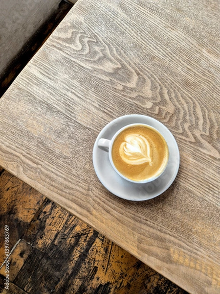 Fototapeta Cup of Cappuccino with Latte Art on Wooden Table in Cozy Cafe