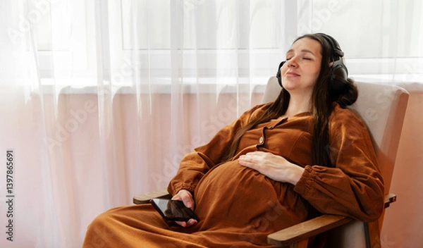 Fototapeta Pregnant woman listening to music with eyes closed at home