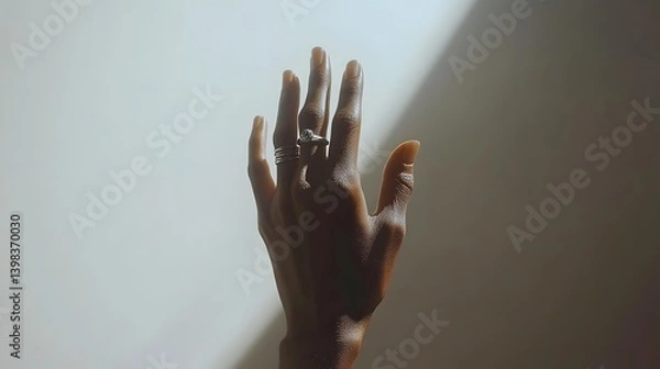 Fototapeta A close-up shot of a dark-skinned hand with rings, reaching up against a white background. Sunlight casts a dramatic shadow.