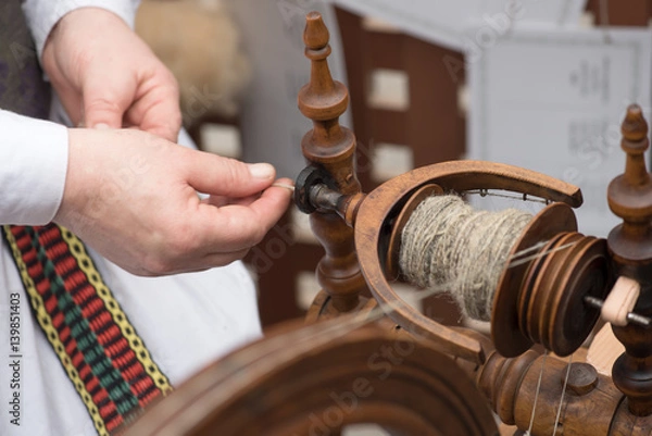 Fototapeta Hands of woman in action spinning line flax with a spinning wheel 
