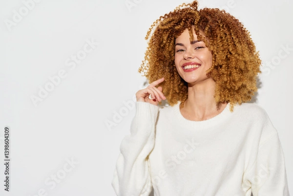Fototapeta Smiling woman with curly hair, wearing a white sweater, against a plain white background, exuding happiness and confidence The soft lighting enhances her joyful expression, making the image warm and