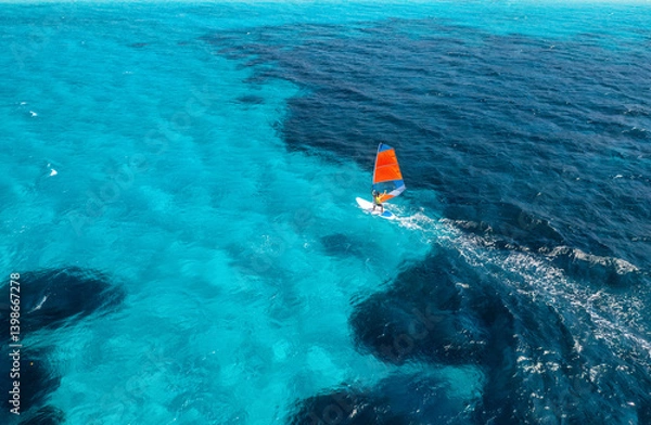 Obraz Aerial view of windsurfer on blue sea at sunny summer day. Windsurfing. Extreme sport and vacation. Top view of man on windsurfer board, waves, clear azure water in Sardinia, Italy. Tropical landscape