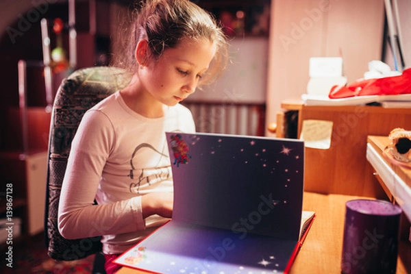 Fototapeta The girl is reading a book sitting at the table