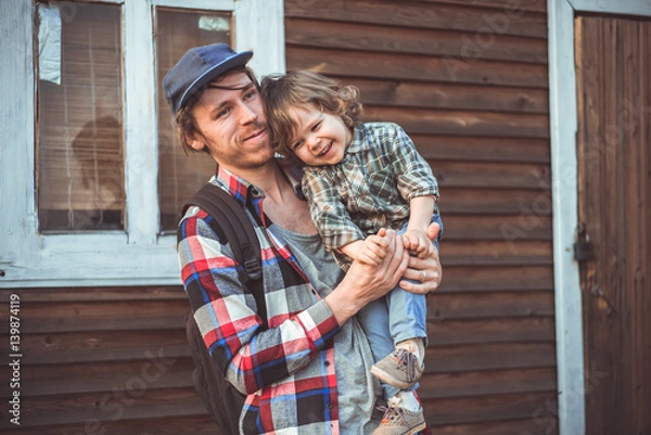 Obraz Папа и сын смеются в клетчатых рубашках на фоне деревянного дома