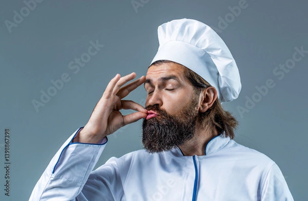 Fototapeta Chef cooker man in apron show sign of good taste, Bellissimo gesture, kiss fingers isolated gray background. Portrait of a happy chef cook. Cook hat. Bearded chef, cooks or baker