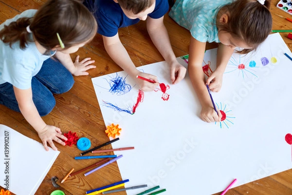 Fototapeta children lying on the floor and drawing. Children draw on a large sheet of paper