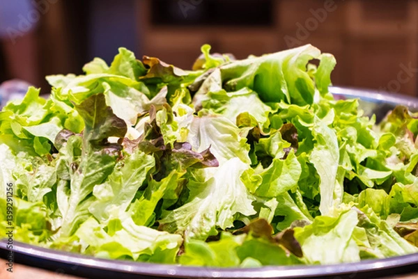 Fototapeta A close-up view of a large metal bowl filled with fresh, mixed green lettuce leaves in a kitchen setting