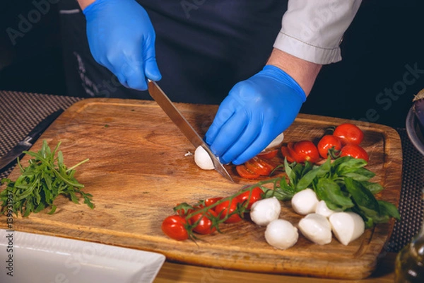 Fototapeta Chef hands with gloves cooked. Chef  is cooking a  gourmet dish - mozzarella with basil, cherry tomatoes and arugula.