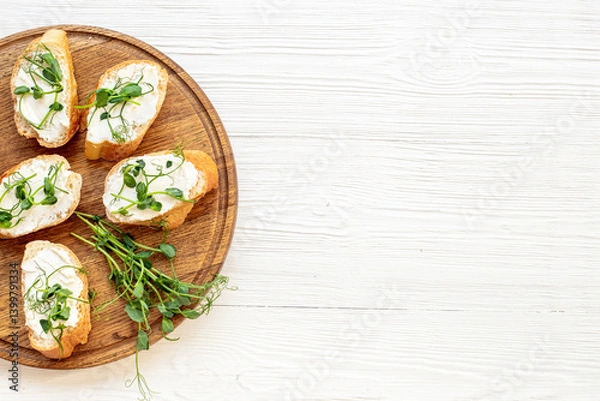 Fototapeta Toasts with fresh sprouting microgreens and cream cheese on wooden board, top view