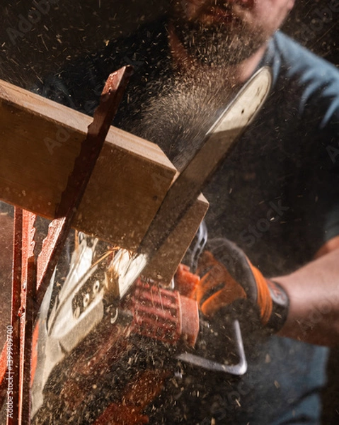 Obraz Worker uses a chainsaw to cut a plank into two pieces while working