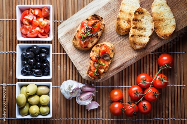 Obraz Bruschetta tomato basil and olives, composition with wooden cutting board top view.