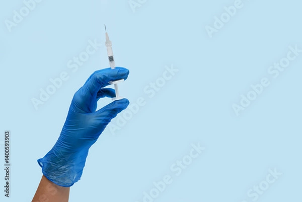 Obraz doctor's hand in gloves holds a medical syringe for injection, syringe in hand on light blue background copy space