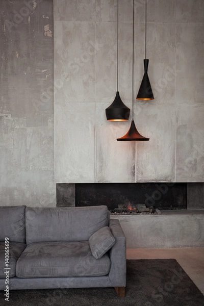 Fototapeta Gray velour sofa in a dark room the bright light from eternal light, and artificial fireplace. Interior loft with concrete walls