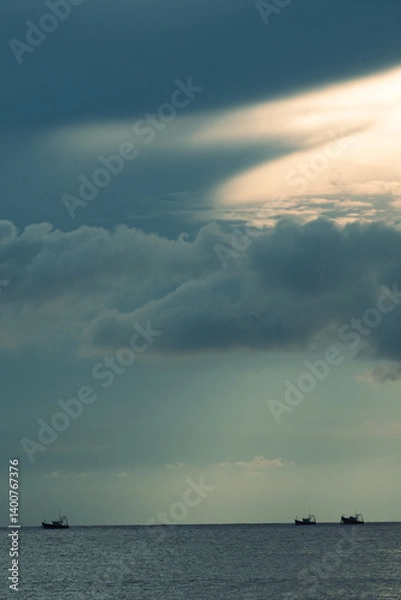 Fototapeta The calm before the storm — fishing boats drift beneath brooding skies as the sun slices through the clouds over the Arabian Sea. Shot in Goa, where the ocean meets poetry.