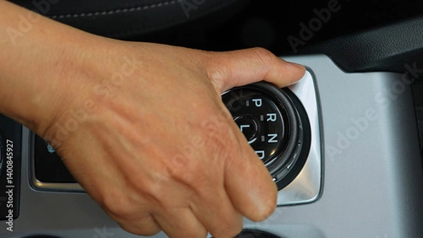 Fototapeta Driver's hand shifts the car gearbox modes such as parking and drive mode and parking brakes. Automatic electronic transmission and gear shift, P Park to D Drive and back in modern cars.