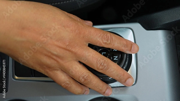 Fototapeta Driver's hand shifts the car gearbox modes such as parking and drive mode and parking brakes. Automatic electronic transmission and gear shift, P Park to D Drive and back in modern cars.