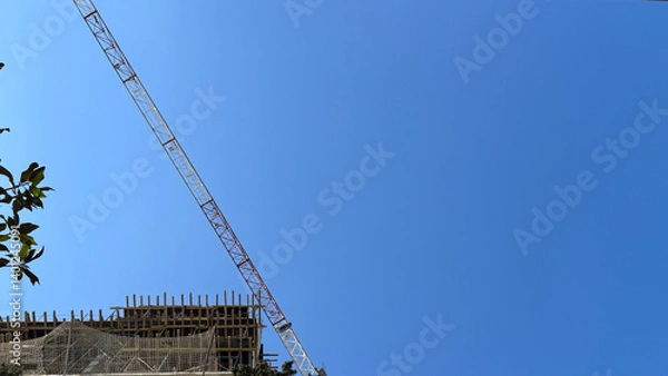 Obraz View of tall construction crane and upper part of building with scaffolding and safety net. Includes copy space.
