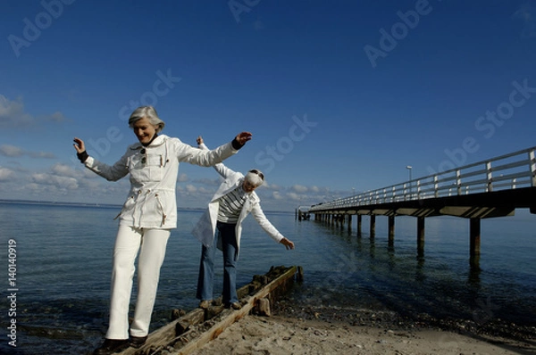 Fototapeta Two mature women balancing over a beam at Baltic Sea beach