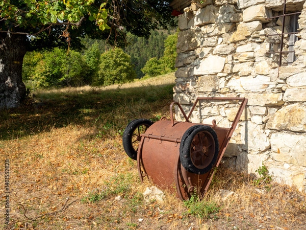Fototapeta rusty bucket on wheels near old stone hut on hills in the Southern Alps in France