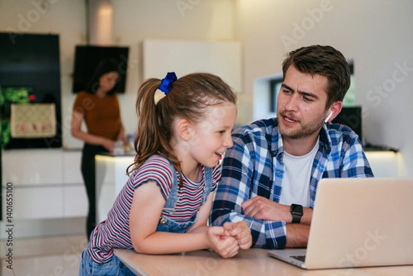 Fototapeta Work from home. Daughter interrupting her father while he is having a business online conversation on his laptop while sitting in the modern living room.