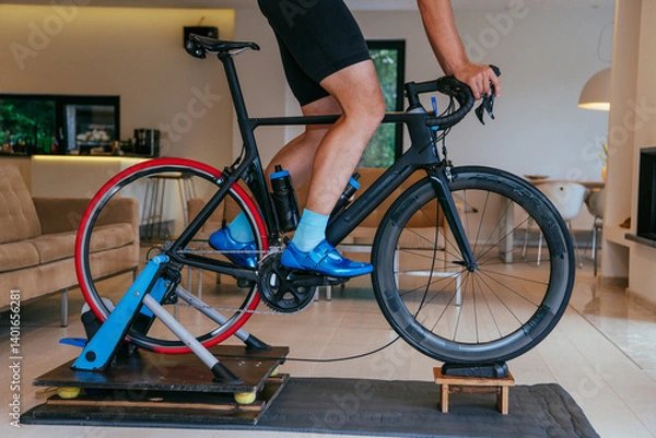 Fototapeta A triathlete riding a triathlon bike on a machine simulation in a modern living room. Training during pandemic conditions.