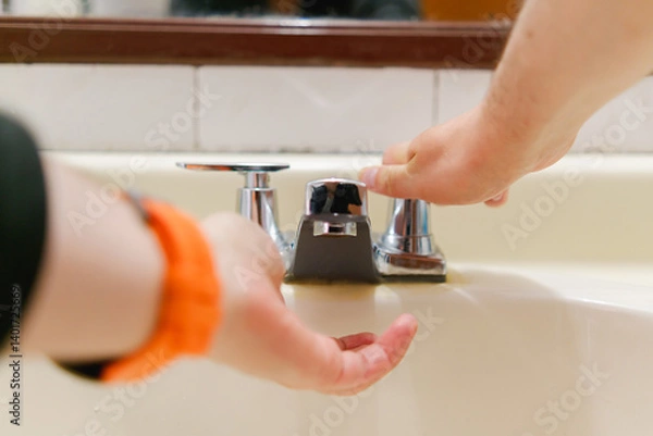 Obraz Two hands use a metal faucet for personal hygiene on a bathroom sink, addressing hygiene and water usage