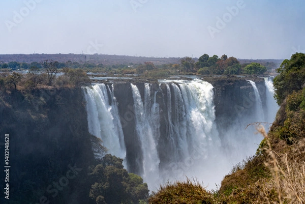 Fototapeta Victoria Falls in Zimbabwe viewed from the side with water cascading down on a sunny blue sky day 