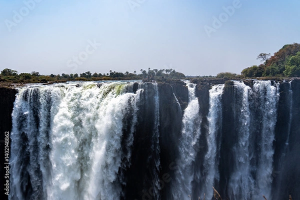 Fototapeta Victoria Falls in Zimbabwe viewed from the front with water cascading down on a sunny blue sky day 