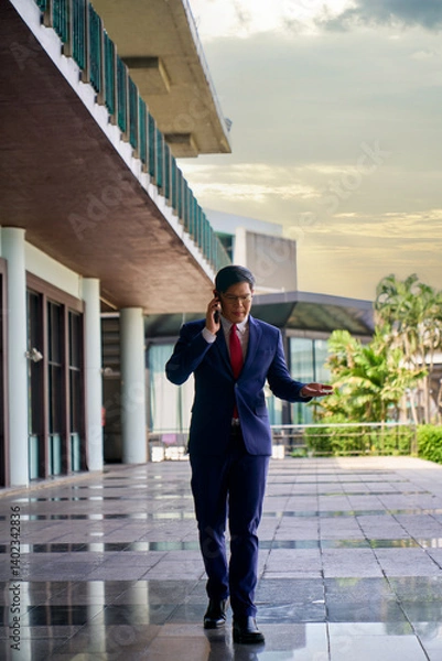 Fototapeta Asian businessman in formal blue navy suit walking and talking with phone in royal club to meeting with partner , Work from anywhere concept.