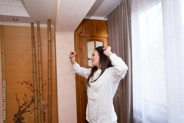 Fototapeta Happy, energetic girl in a white sweatshirt and black leggings dancing at home