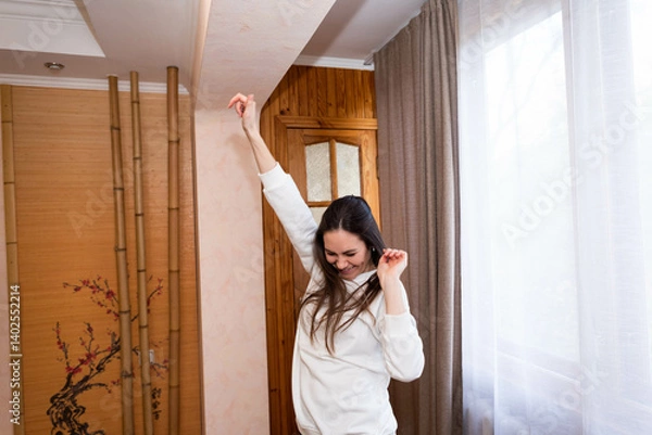 Fototapeta Happy, energetic girl in a white sweatshirt and black leggings dancing at home