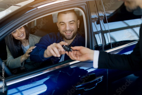 Fototapeta Smiling millennial couple receiving car keys from salesman while sitting inside their newly purchased car in dealership showroom, happy spouses buying modern vehicle in auto salon, closeup