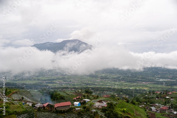 Fototapeta Scenic view of Mount Marapi with clouds hovering above lush green villages and terraced fields in West Sumatera, Indonesia. 