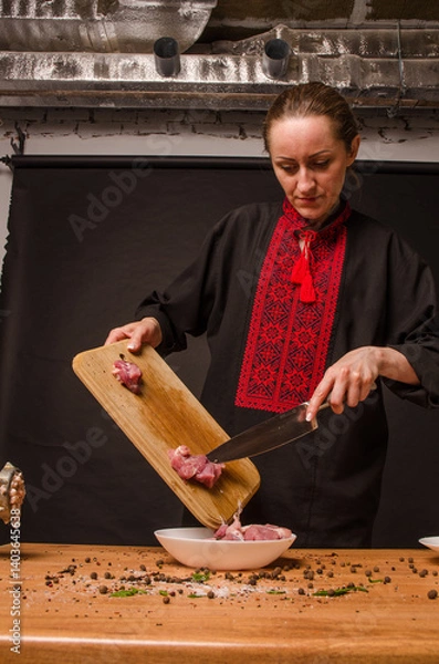 Fototapeta Female chef cuts raw chicken meat on a round wooden Board. The view from the top. Cook chef hands woman cuts raw meat chicken breast on a wooden background