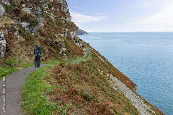 Fototapeta Backpacker walks on the South West Coast Path in North Devon out of Lynton and along a section called the Valley of Rocks