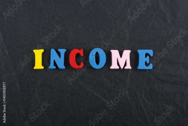 Obraz INCOME word on black board background composed from colorful abc alphabet block wooden letters, copy space for ad text. Learning english concept.