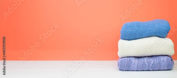 Obraz Knitted woolen sweaters. A bunch of knitted winter, autumn clothing on an orange background, sweaters, knitwear, space for the text. Banner.