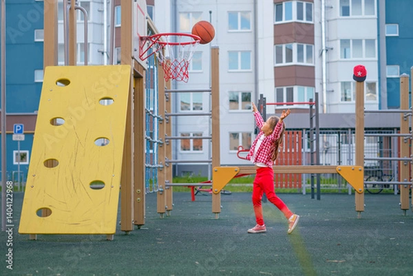 Obraz A girl on the playground makes a well-aimed throw with a basketball into a basketball hoop