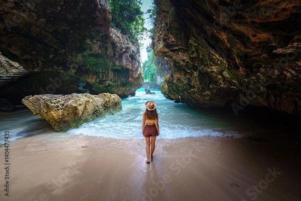 Obraz Back of girl traveler wearing hat on the beach among the rocks on Bali island. Journey to a beautiful destination