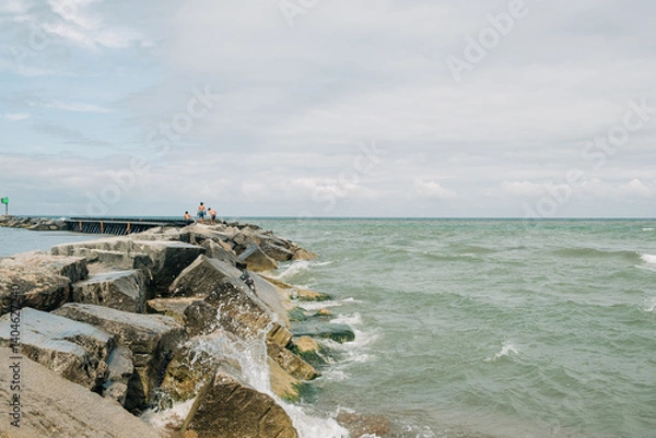 Obraz Waves crash against rocks while people enjoy a coastal walk