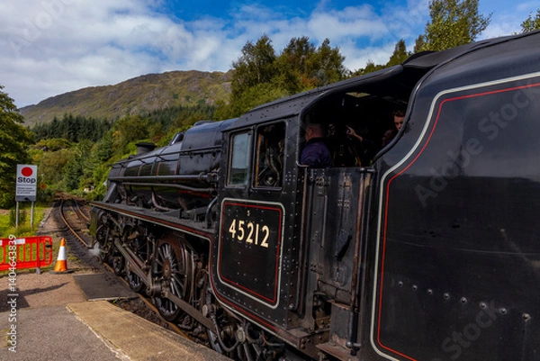 Fototapeta Iconic Jacobite steam train crosses Glenfinnan Viaduct and stops at the station, with historical details, smoke, and nostalgia. Timeless and magical icon in the Scottish Highlands. Locomotive interior