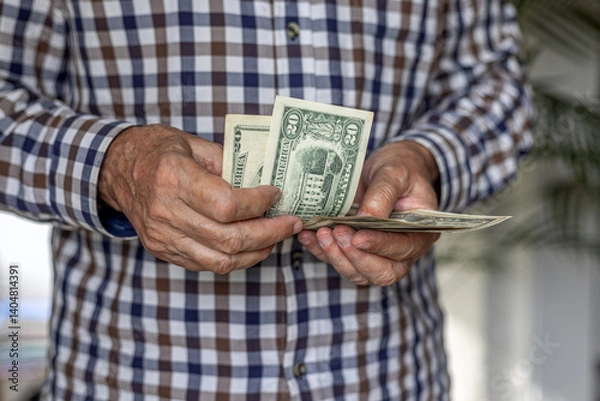 Fototapeta Frontal close-up of a man counting a wad of American Dollar banknotes, in 20 dollar denomination. Cash in hand concept - wages, payment, dividends, investment, austerity, loan or winnings.