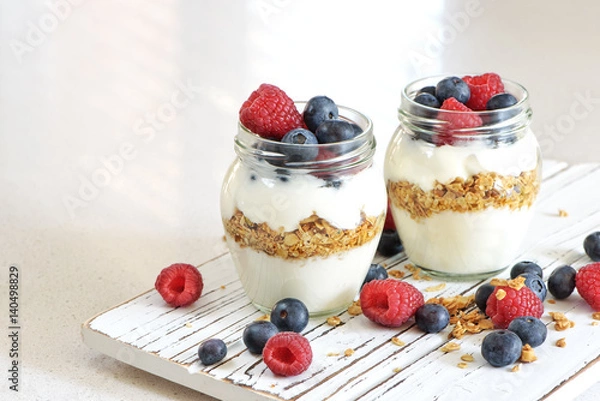 Obraz Yogurt with bluberry and raspberry in the glass jars with berries around on the wooden board